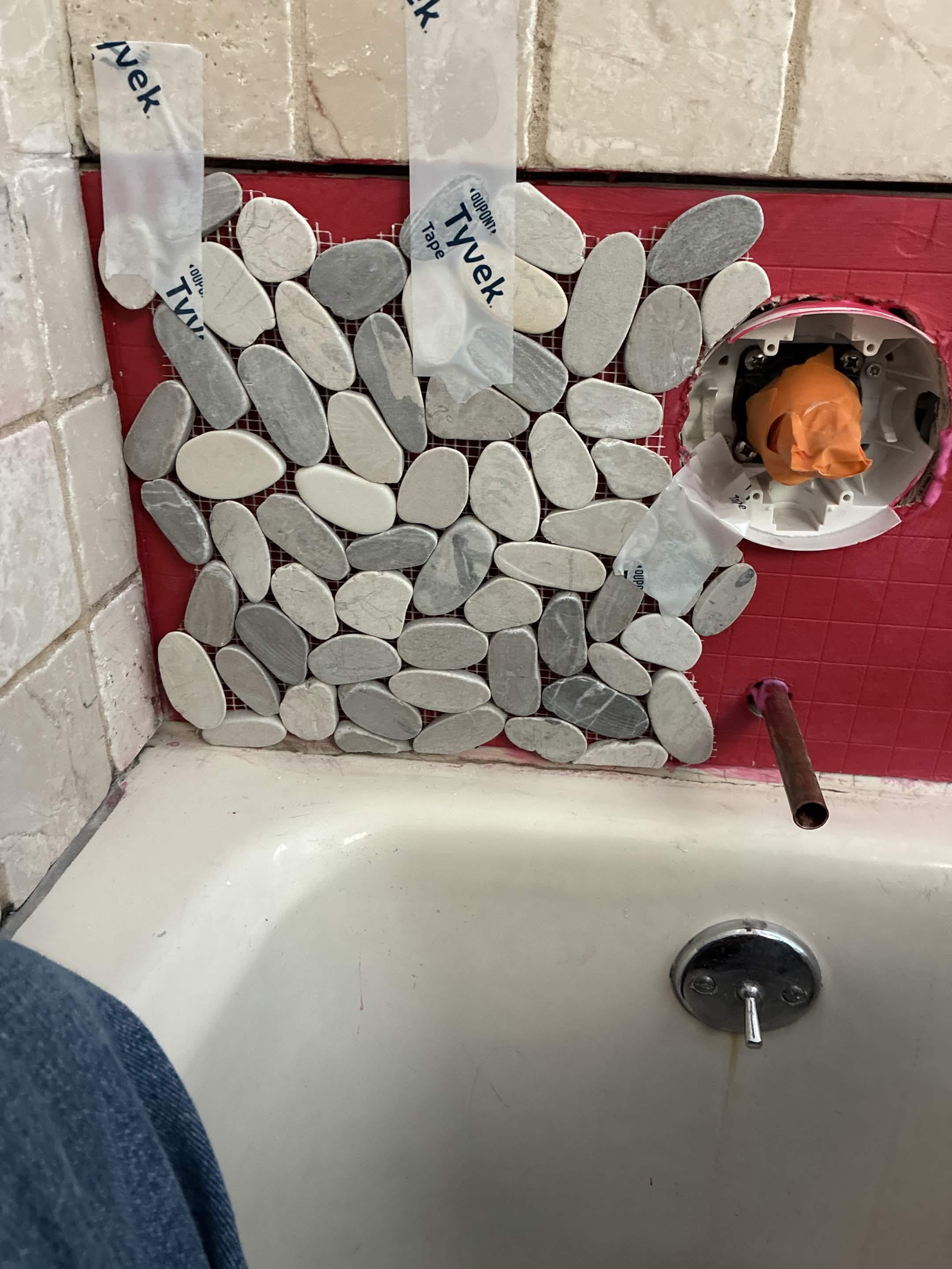 Pebble mosaic tile being set on tub surround with Tyvek tape holding stones