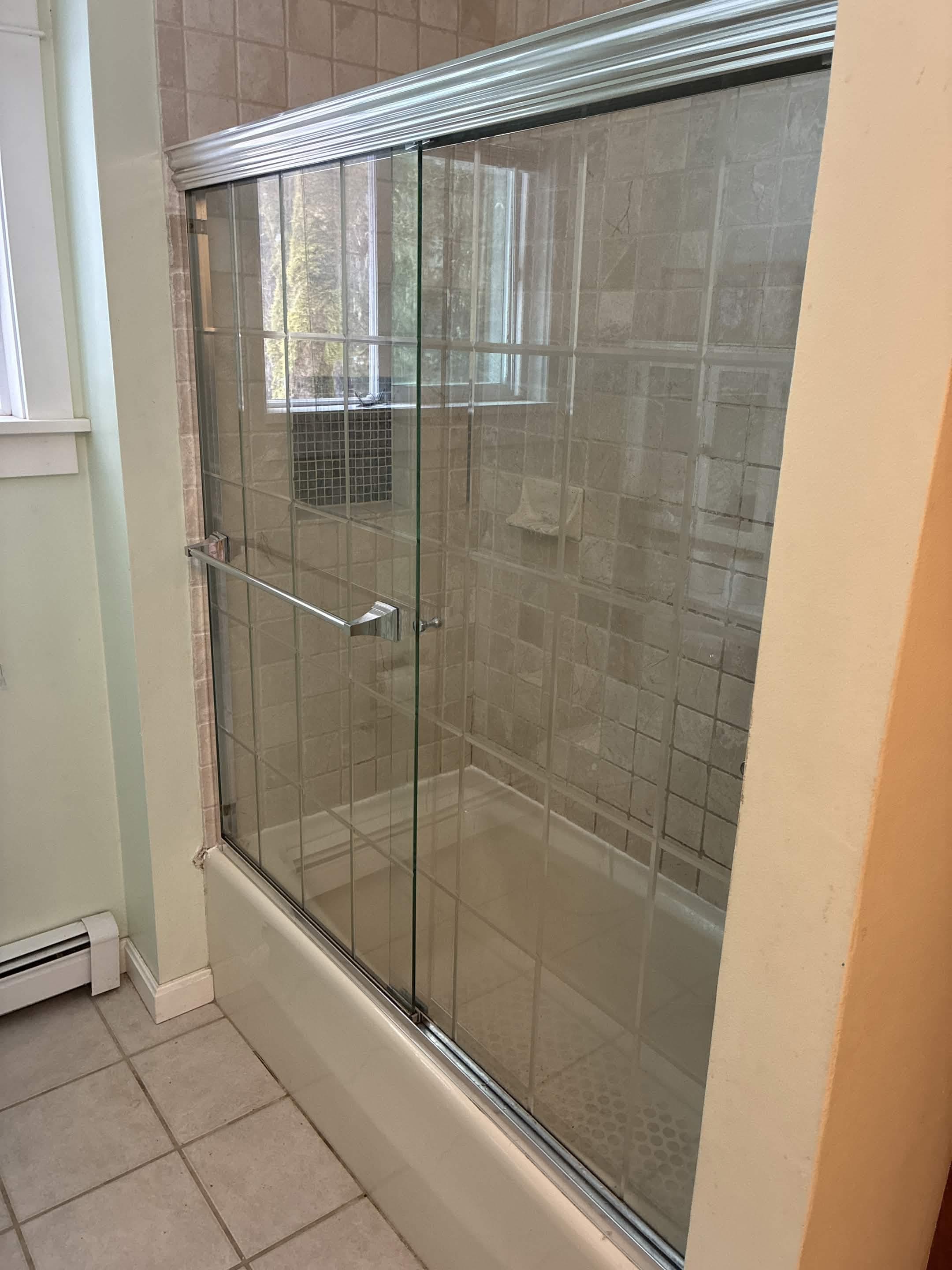 Finished bathroom with travertine tile surround and new glass sliding shower door