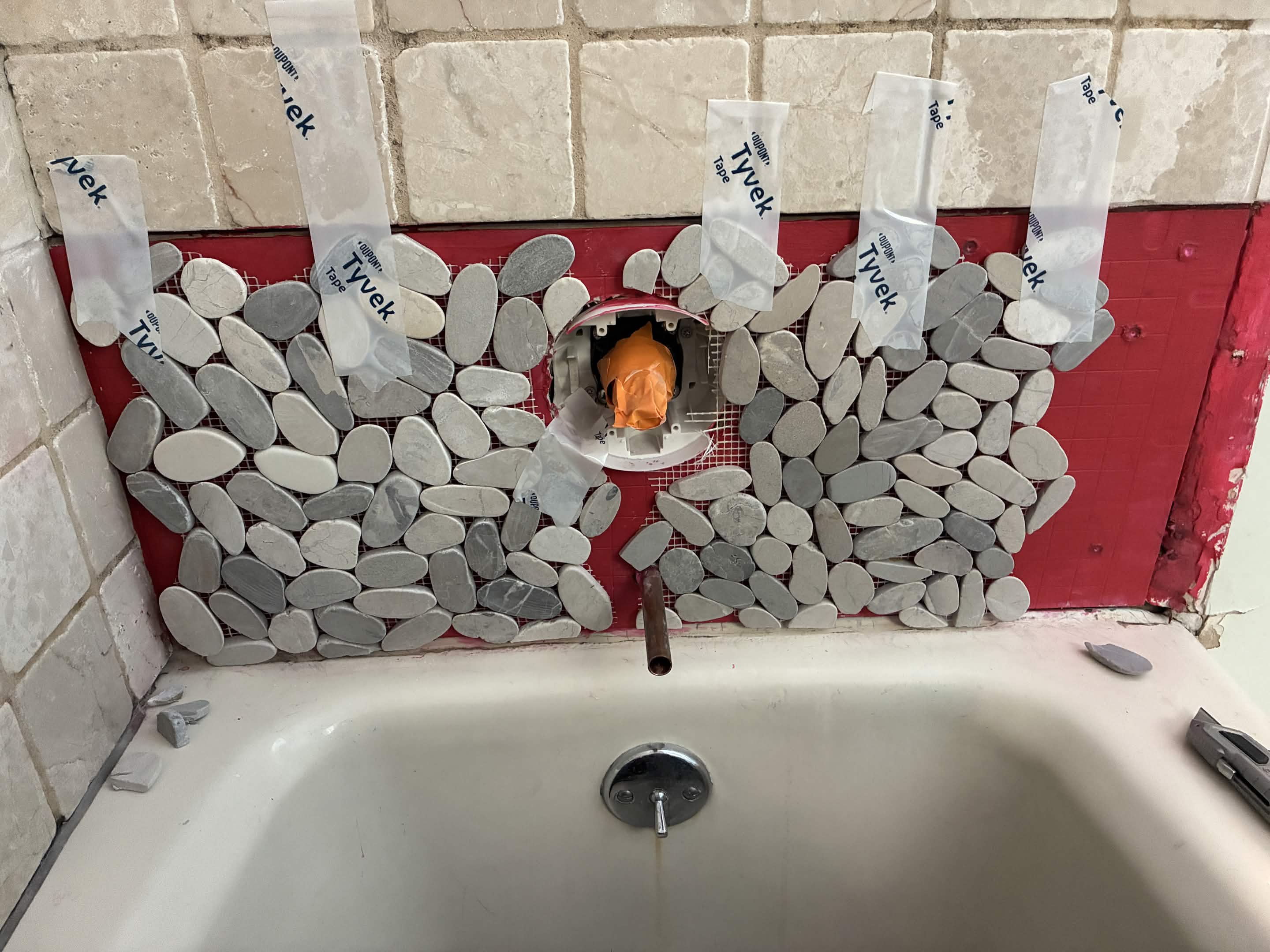 Pebble mosaic band set with tape, prepped for grout on tub surround